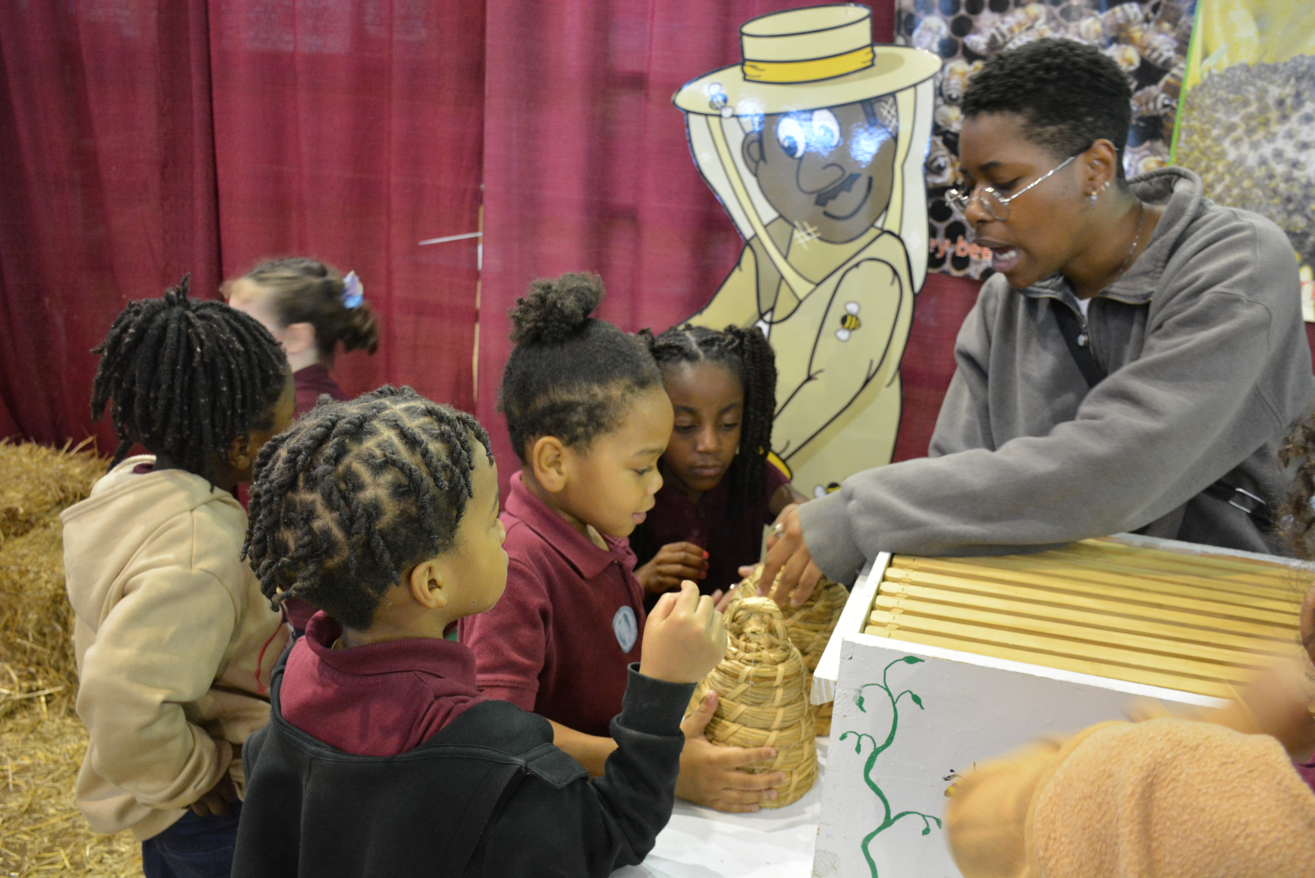Children gathered around a table with a beekeeping display, guided by an instructor.